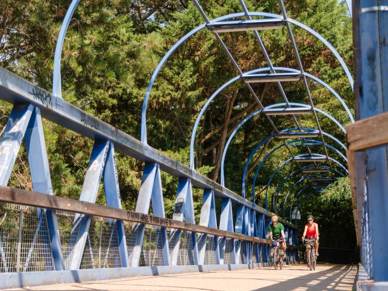Deux cyclistes traversent la passerelle métallique bleue de la coulée verte du sud parisien, voie verte de la Véloscénie au départ de Paris.