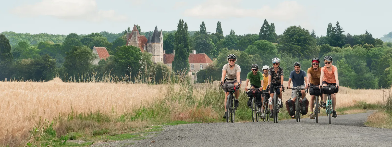 Cyclistes roulant sur une route avec vue du manoir de la Vôve en arrière-plan
