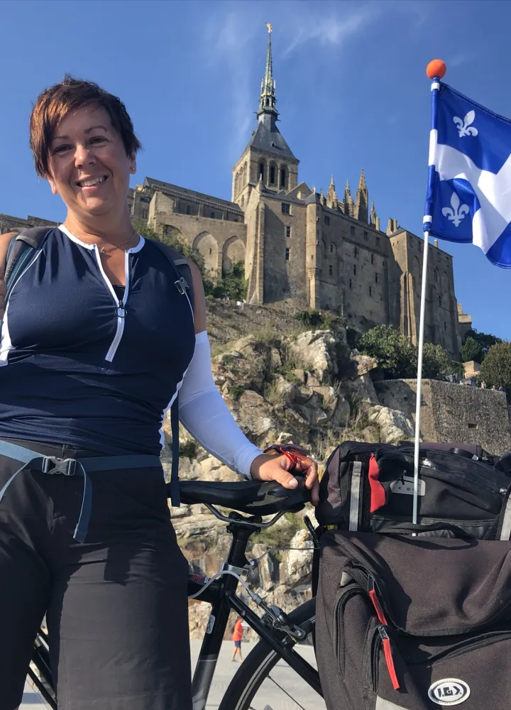 Josiane et son vélo orné d'un drapeau du Québec à son arrivée au Mont Saint-Michel le long de La Véloscénie