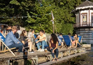 Des personnes assises dans des transats prennent un verre au bord de l'eau à la guinguette de Chartres.