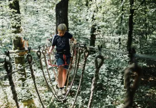 Un garçon traverse un pont de singes en hauteur dans l'accrobranche de Bagnoles de l'Orne