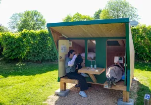 2 personnes se reposant devant une cabane étape au camping